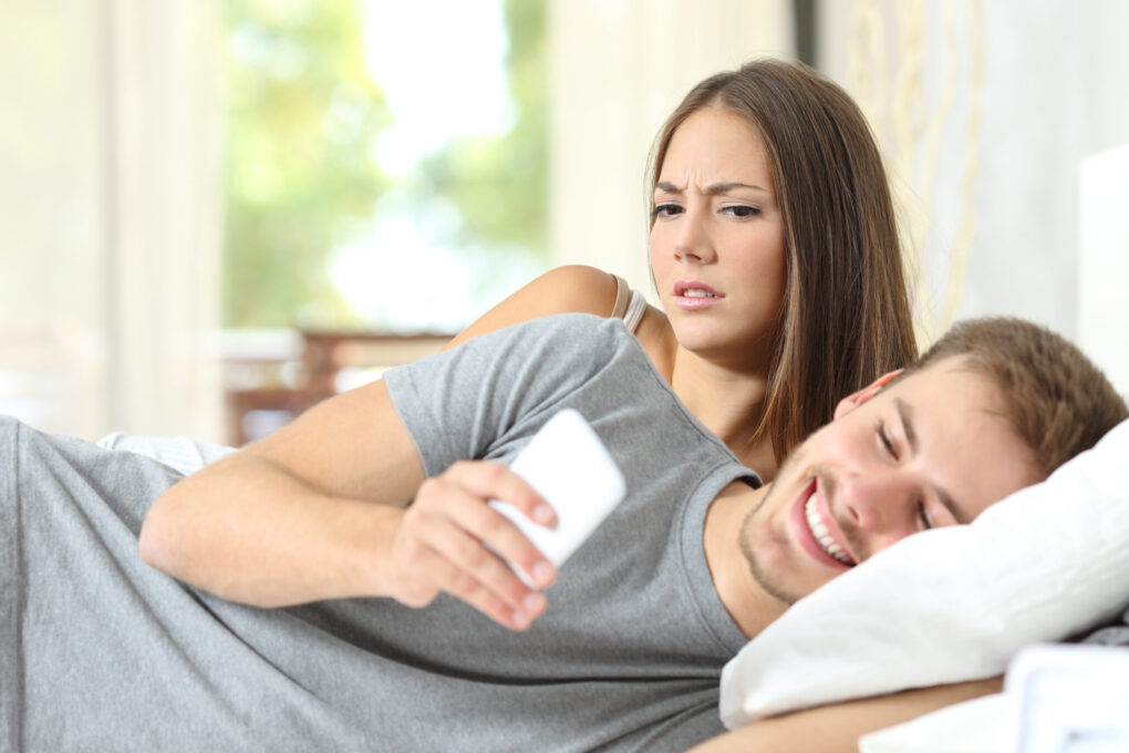 Suspicious woman watching her husband read a message on his phone | Source: Shutterstock